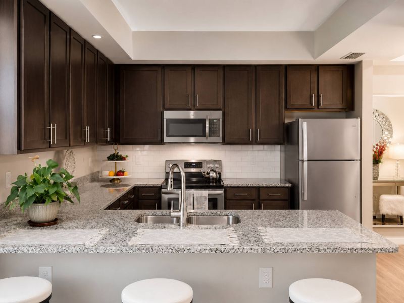 Modern kitchen with dark cabinets, stainless steel appliances, and a granite countertop with three white stools.