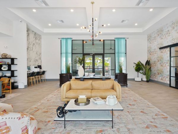 Modern lounge with a tan sofa, coffee table, accent chairs, and large windows with teal curtains.